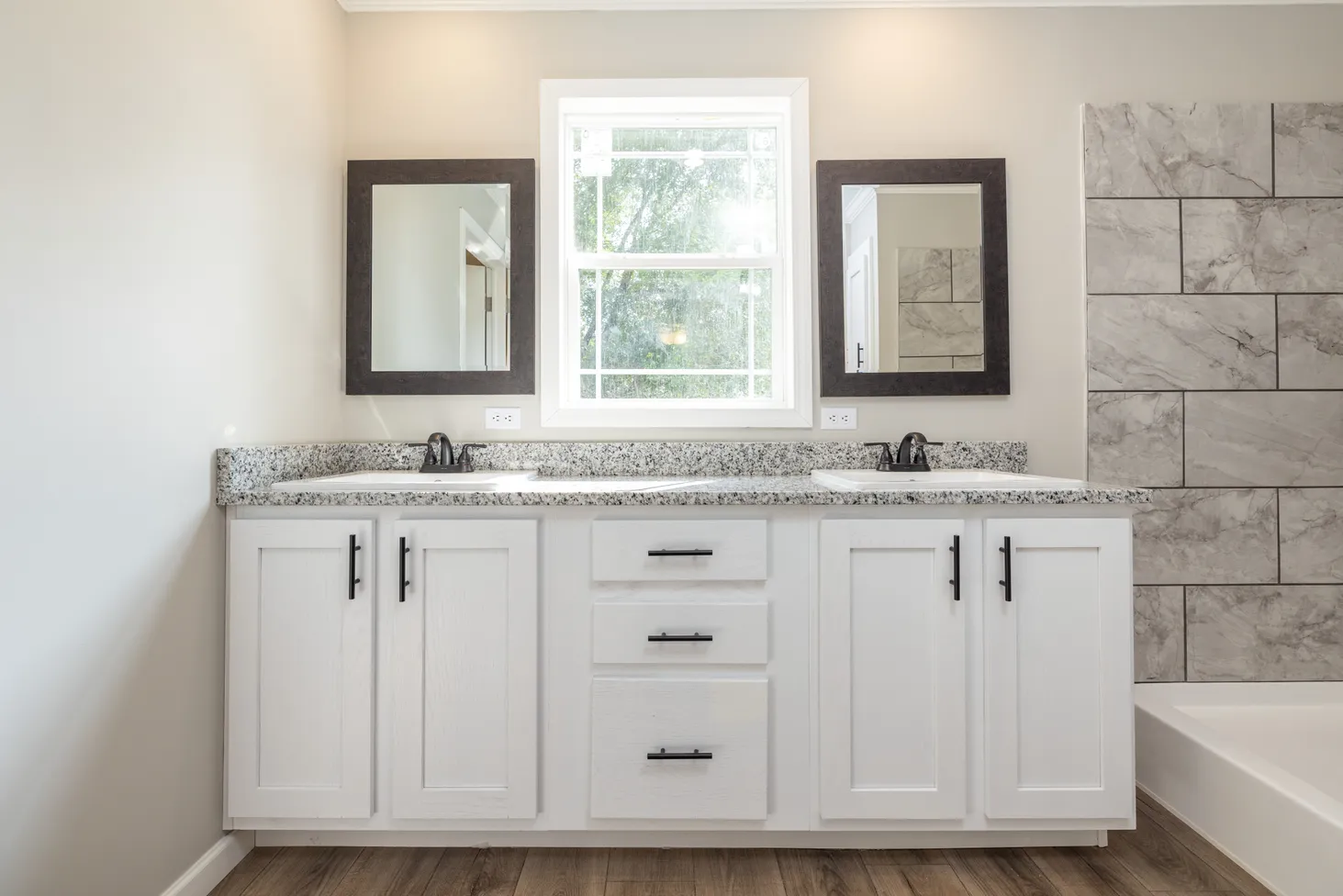 Double sinks with black-and-white speckled countertops, white cabinets, and marble-textured shower tiles